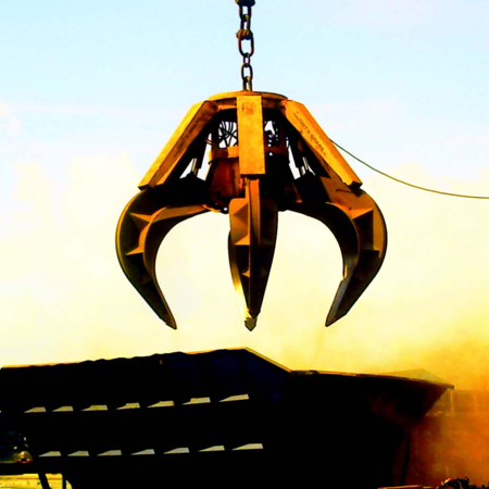 Electro-hydraulic orange peel grab type EHM at sunrise on an industrial site. The swirling dust is illuminated by the sun