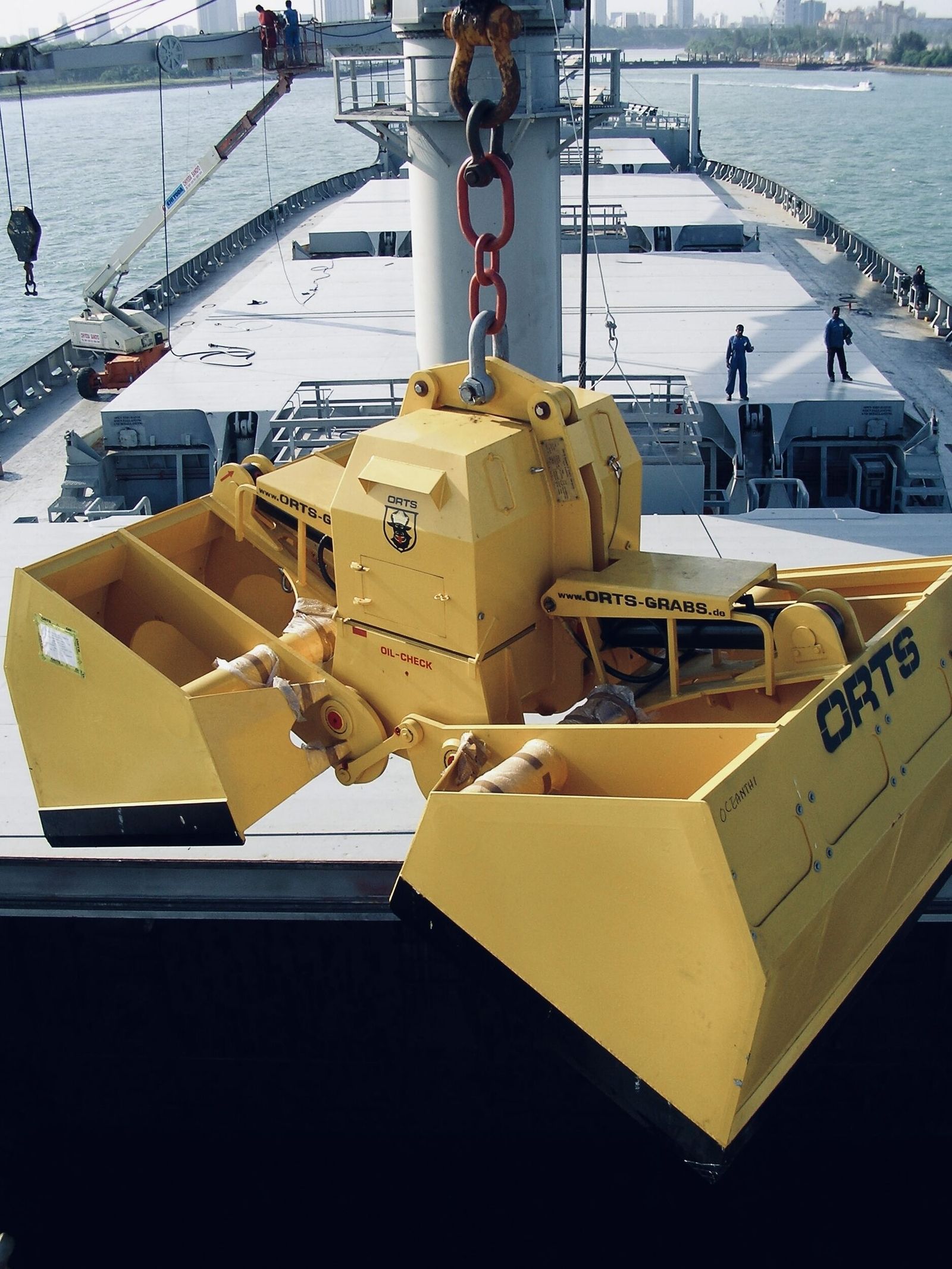 Elektro-hydraulischer Zweischalengreifer auf einem Schiff, während 2 Arbeiter in der Nähe überwachen und sicherstellen, dass alles ordnungsgemäß verläuft